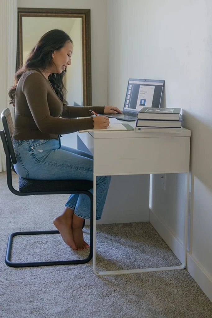 A student studies at a desk by a window.