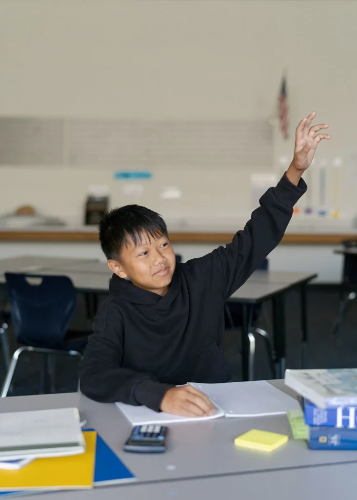 A student raises his hand beside his notebook.