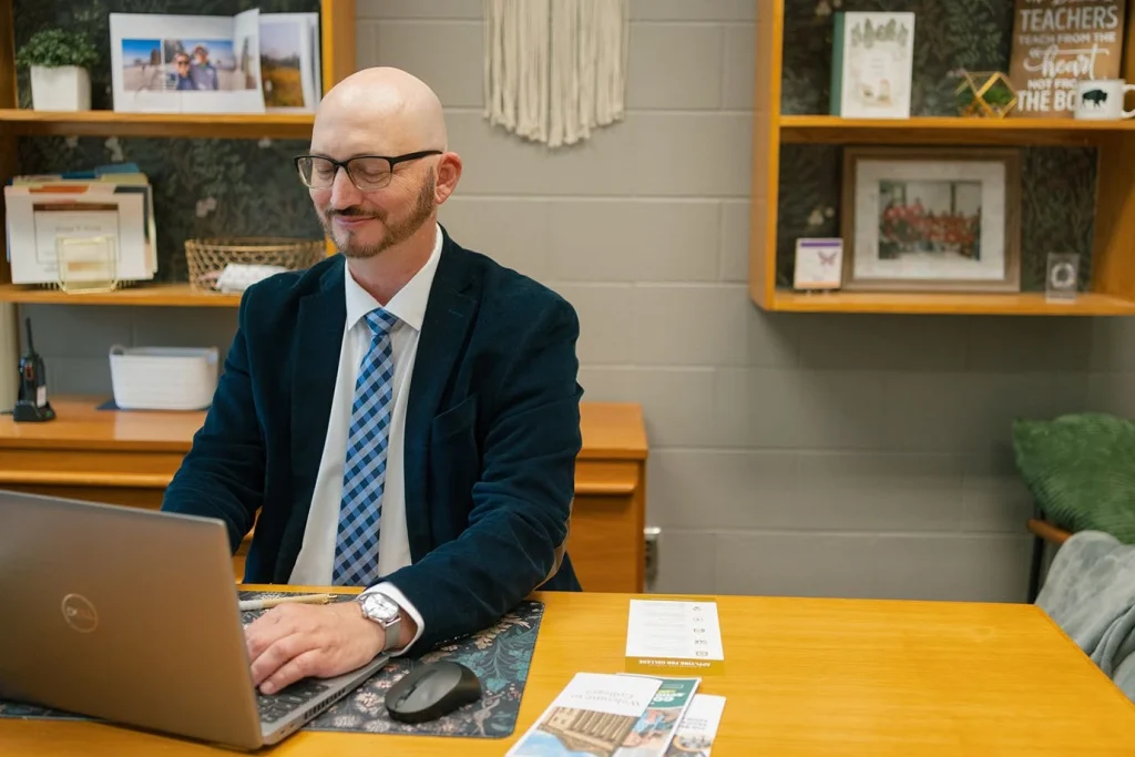 An adviser works at a laptop with college planning materials nearby.