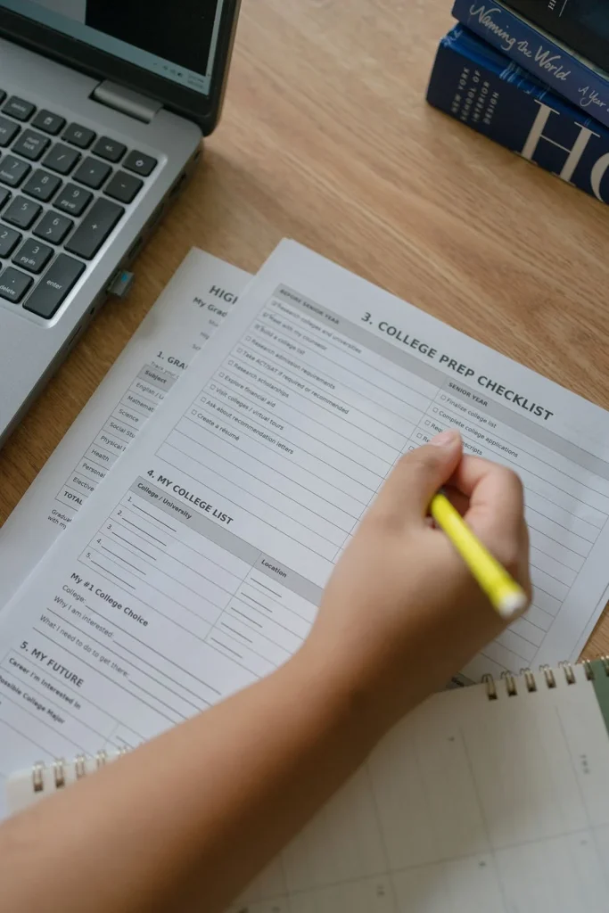 A student writes on a planning worksheet beside a laptop.