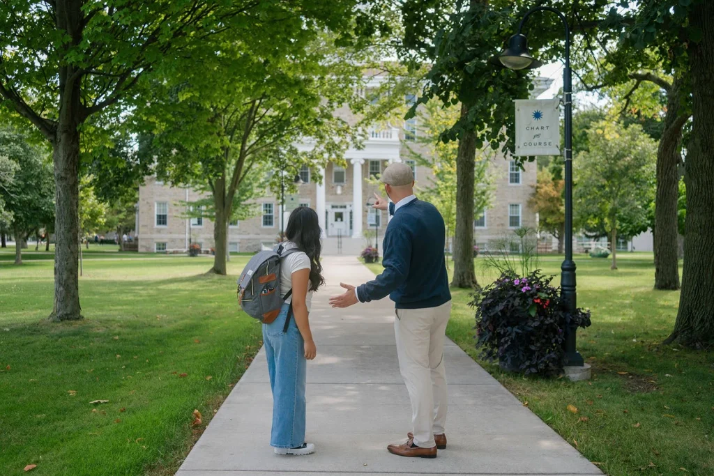 A student and an adult talk while walking on a college campus.