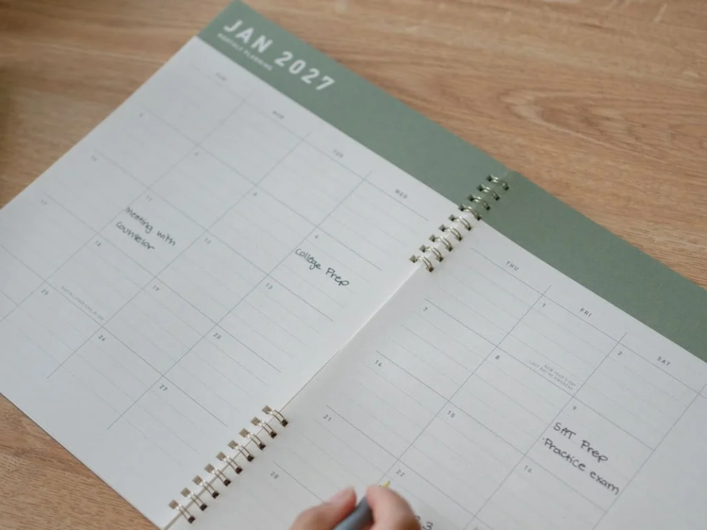 A student writes in a planner beside course materials.