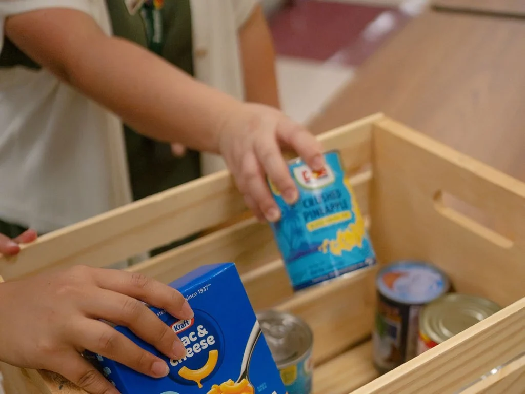 Hands place donated food into a collection box.